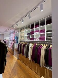 Rayonnages et cintres de pulls en maille violet, beige et gris dans une boutique de mode lumineuse.