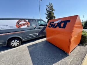 Van TVS34 Tous Vos Services dépannage serrurerie à côté d'un bac orange SIXT dans un parking ensoleillé.