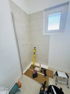Installation d'une douche avec carrelage beige, niveau, perceuse et outils de rénovation sur le sol.