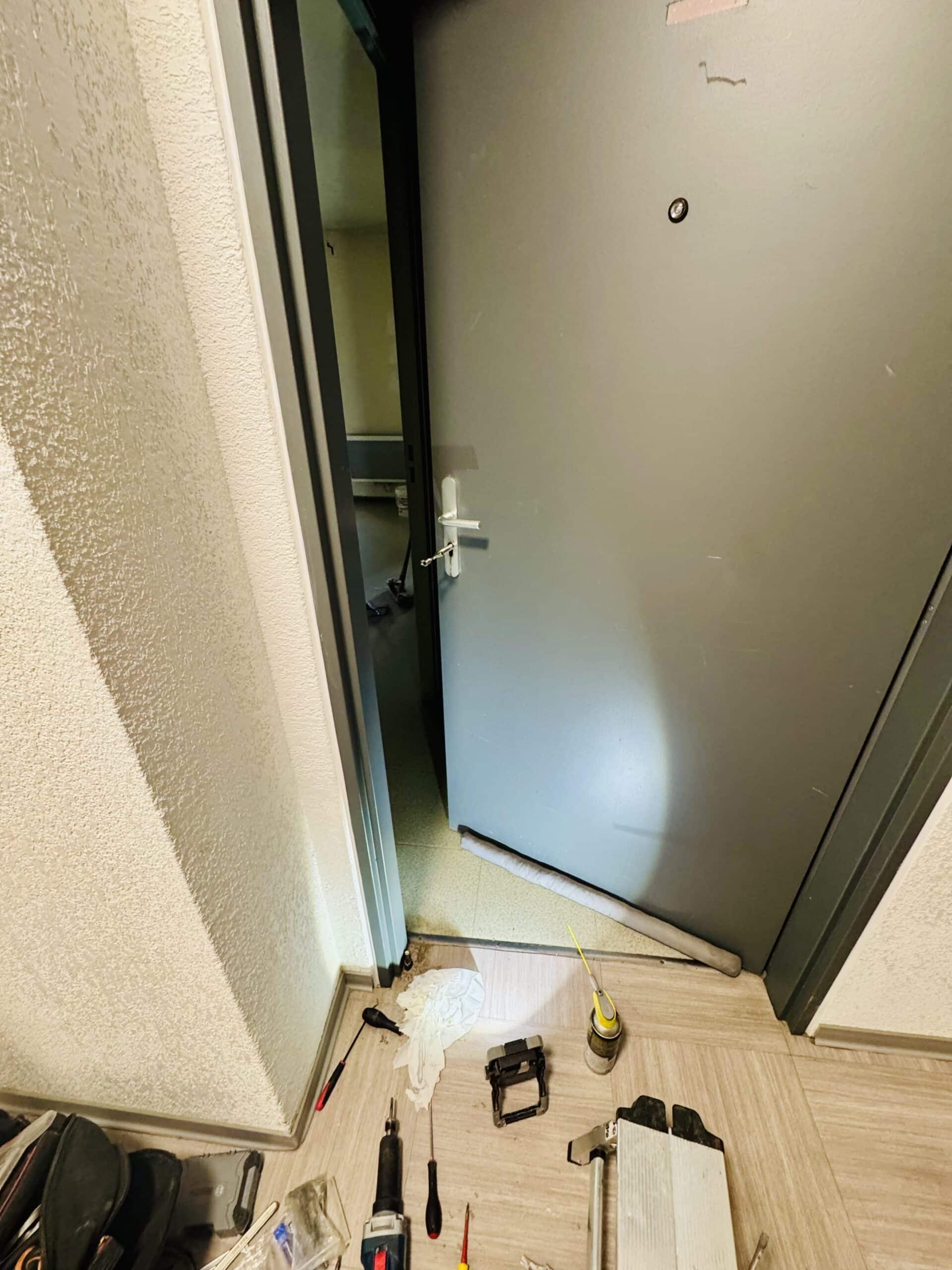 Installation d'une porte grise avec outils de bricolage au sol, perceuse et tournevis dans un appartement.