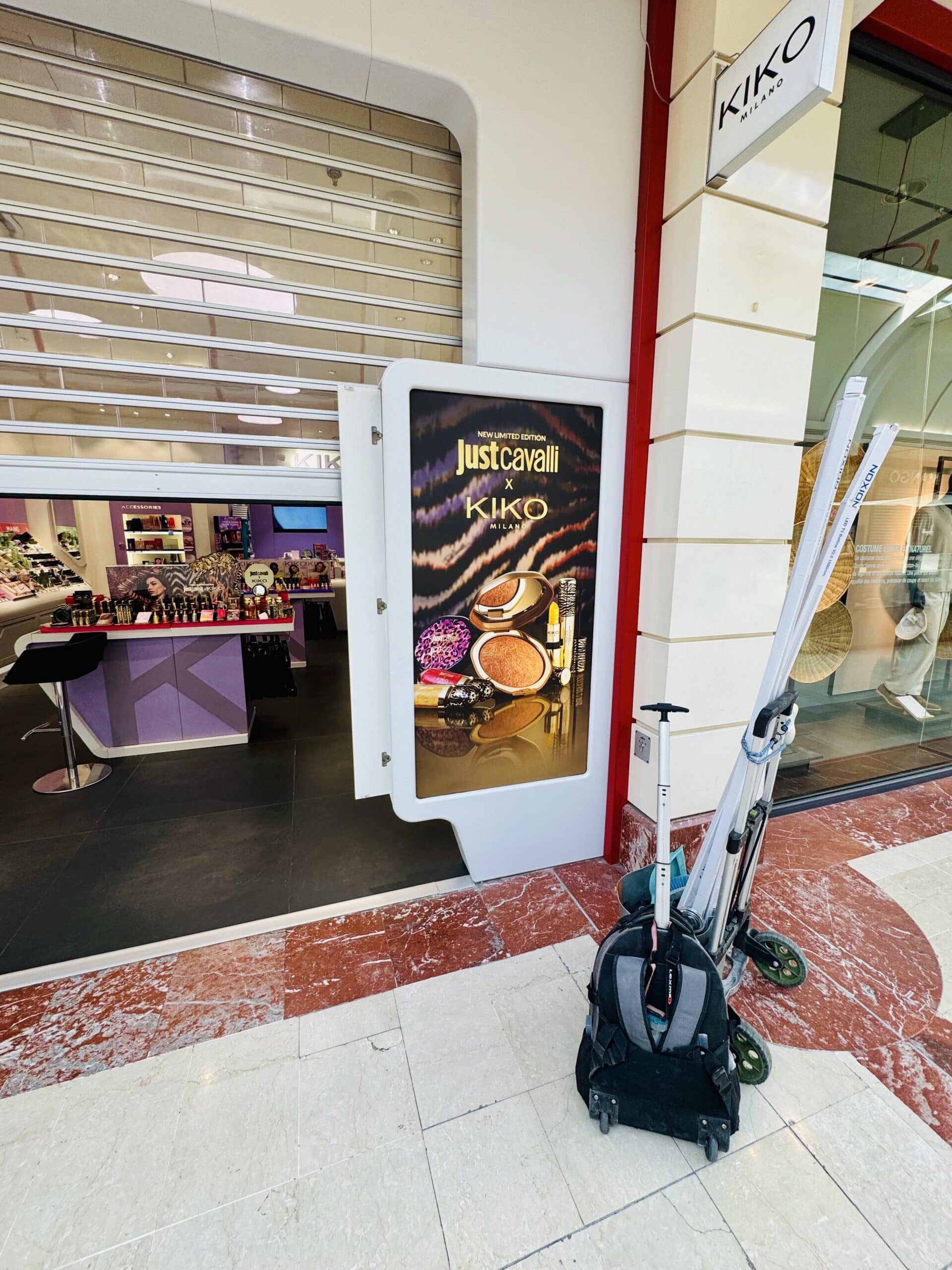 Publicité Just Cavalli x KIKO Milano sur une vitrine de boutique avec un chariot d'entretien au premier plan.