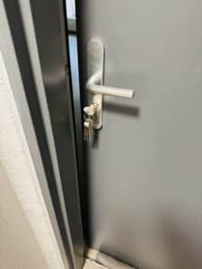 Porte grise entrouverte avec poignée argentée et trousseau de clés inséré dans la serrure.