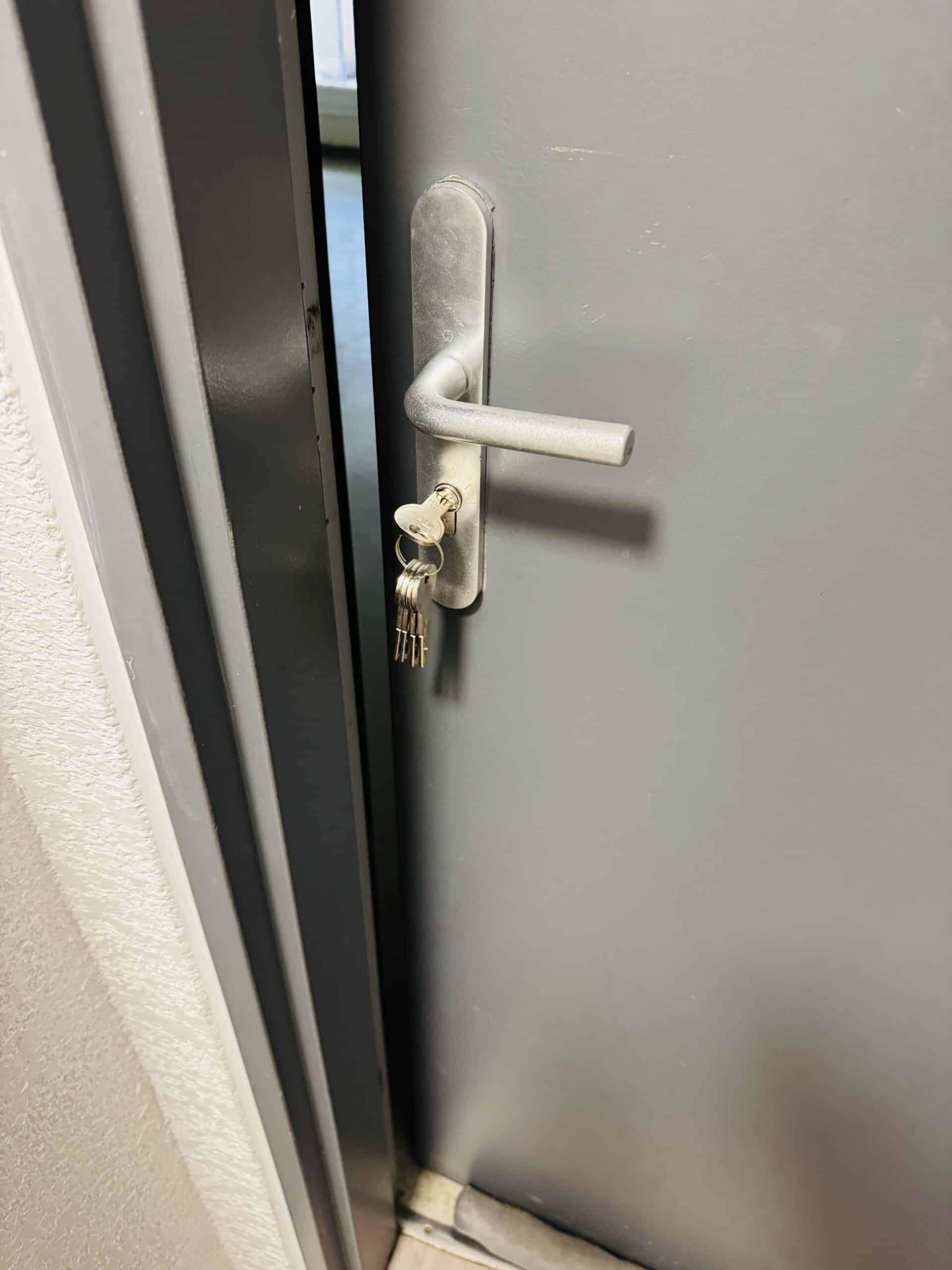 Porte grise entrouverte avec poignée argentée et trousseau de clés inséré dans la serrure.