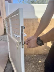 Homme ajustant la serrure d'un portillon en métal blanc avec une clé Allen, clés pendantes.