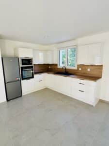Cuisine moderne blanche et bois, électroménager Beko, plan de travail chêne, évier noir et carrelage gris.