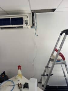 Climatiseur Mitsubishi ouvert pour maintenance avec échelle Hailo, tuyaux et produits de nettoyage.