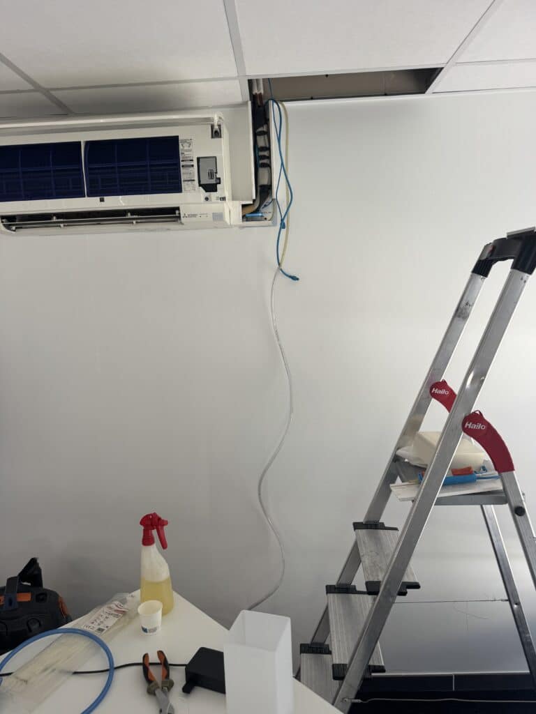 Climatiseur Mitsubishi ouvert pour maintenance avec échelle Hailo, tuyaux et produits de nettoyage.