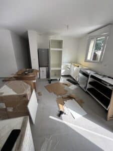 Cuisine Howdens en montage avec meubles blancs, outils et cartons sur carrelage gris.