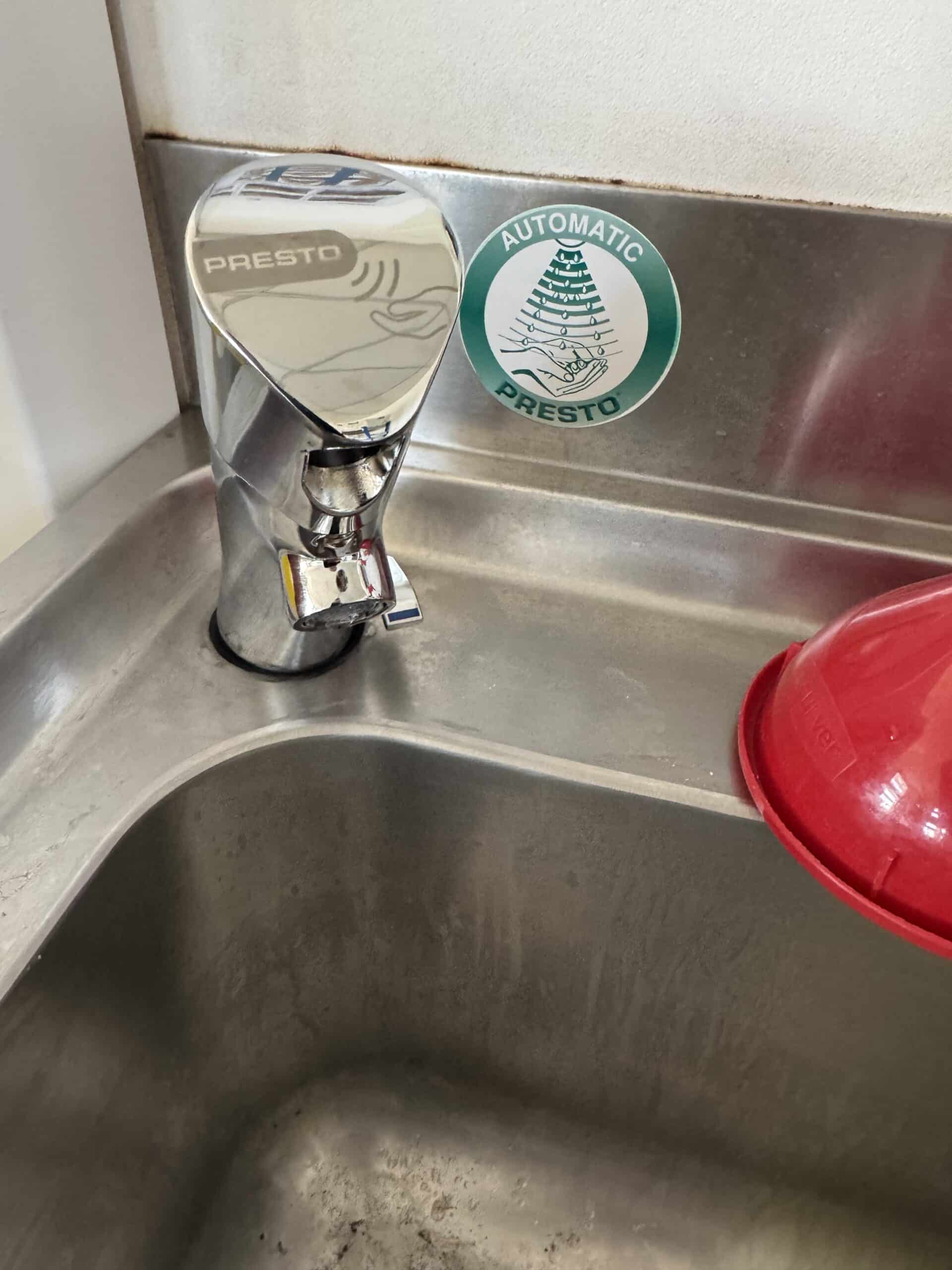 Robinet chromé automatique Presto sur évier inox avec sticker "Automatic Presto" vert et blanc.