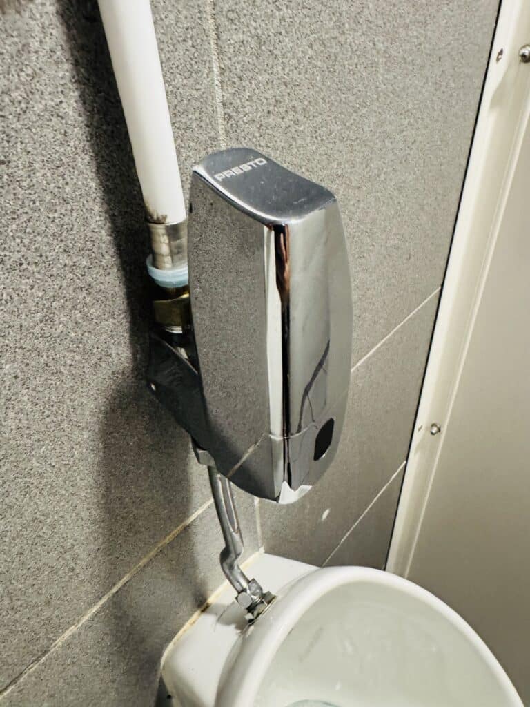 Robinet de chasse automatique Presto chromé sur mur gris pour urinoir.