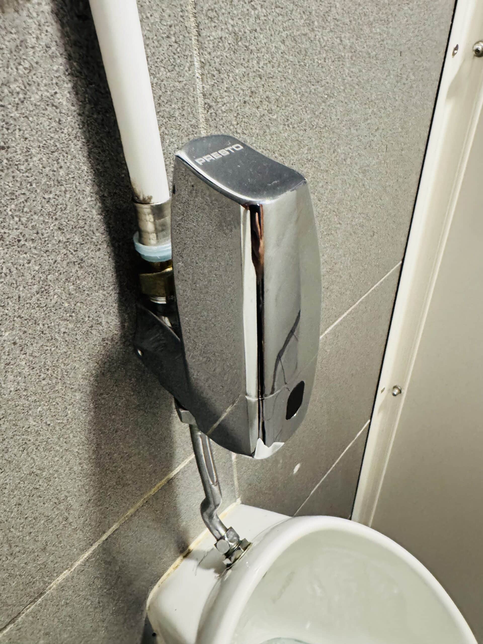 Robinet de chasse automatique Presto chromé sur mur gris pour urinoir.