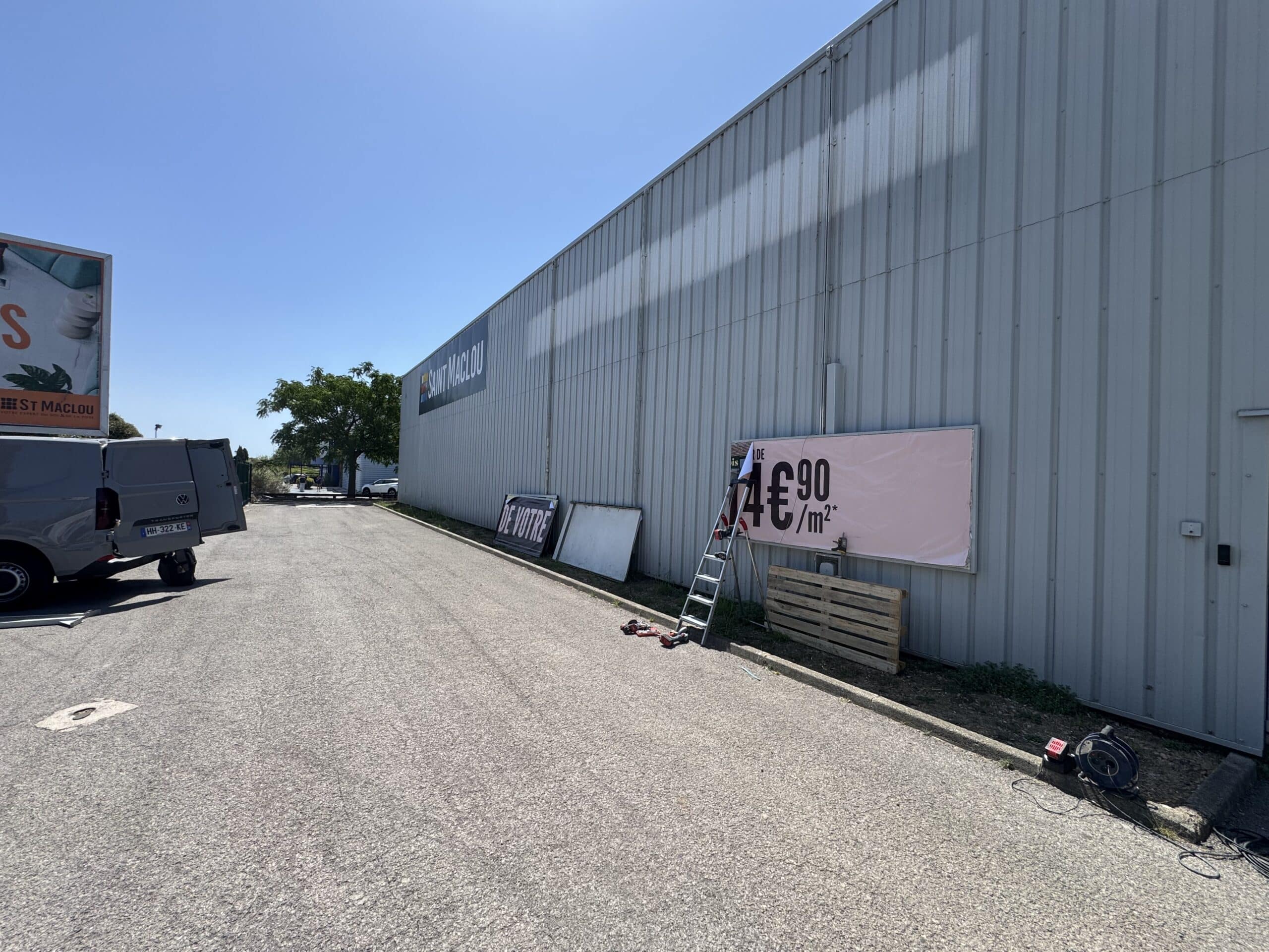 Bâtiment Saint Maclou avec camionnette, échelle et affiche promotionnelle de 4€90/m² sur façade grise.