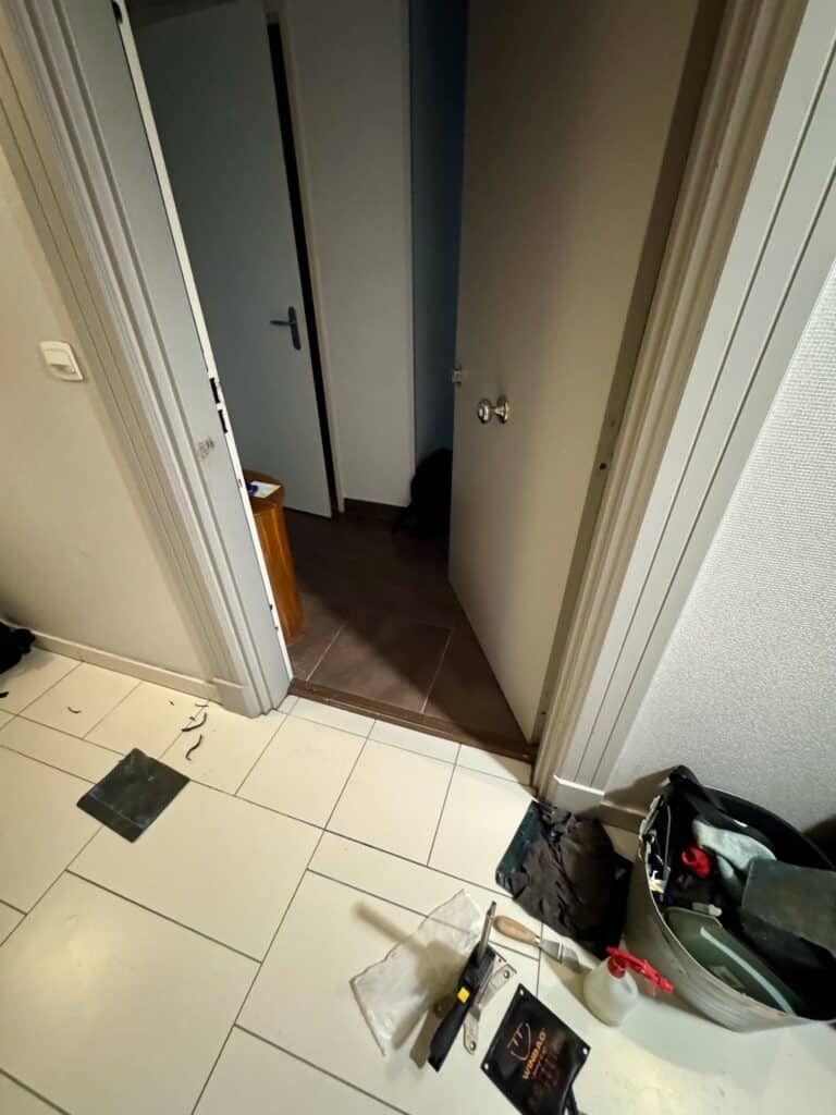 Coussin Winbag et outils de bricolage sur carrelage blanc, porte ouverte révélant un chat noir caché.
